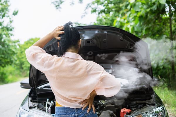 woman having problem with broken, overheat car while driving alone on the road standing with smoke